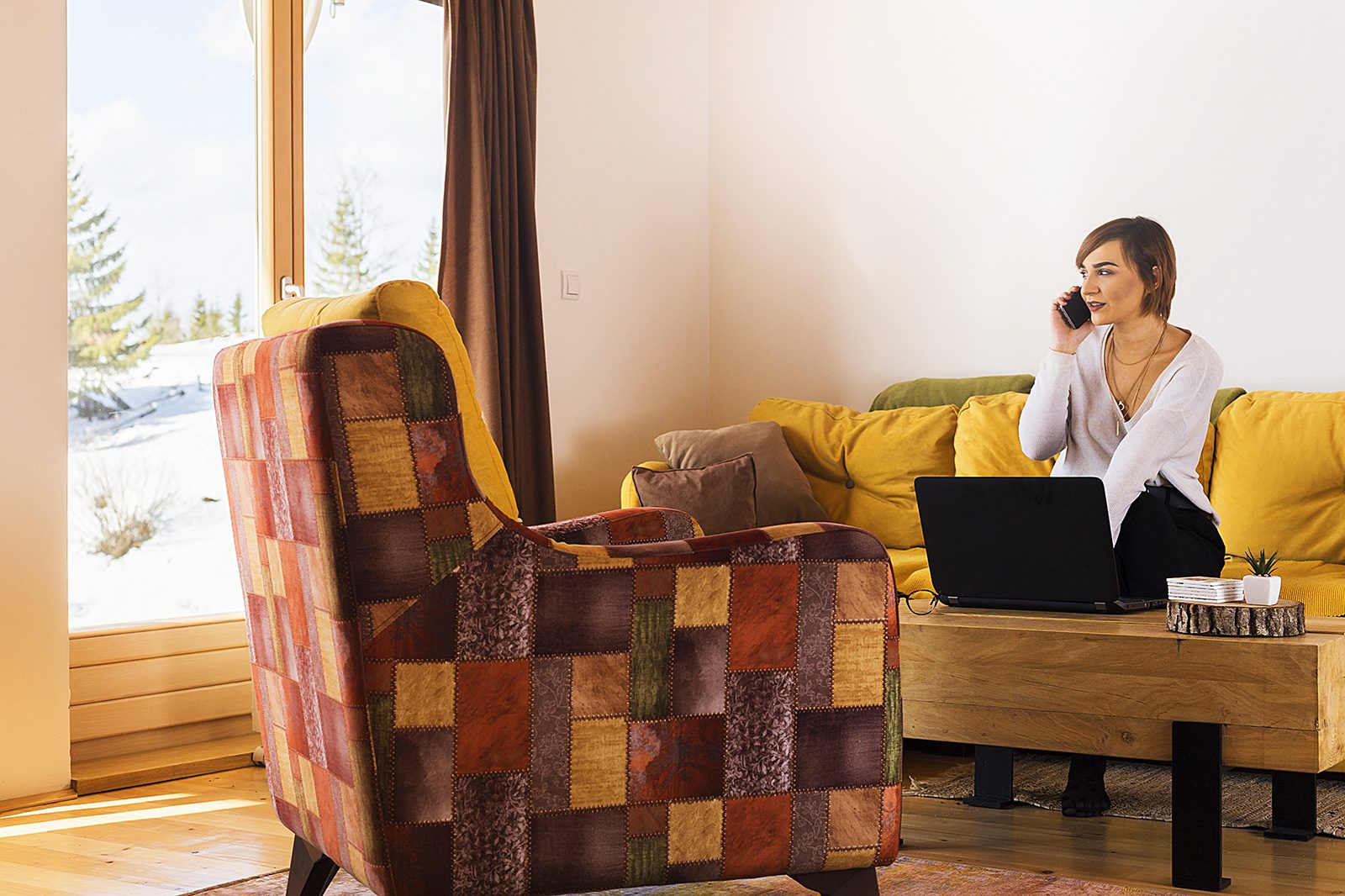 A woman sits on her couch while talking on the phone.