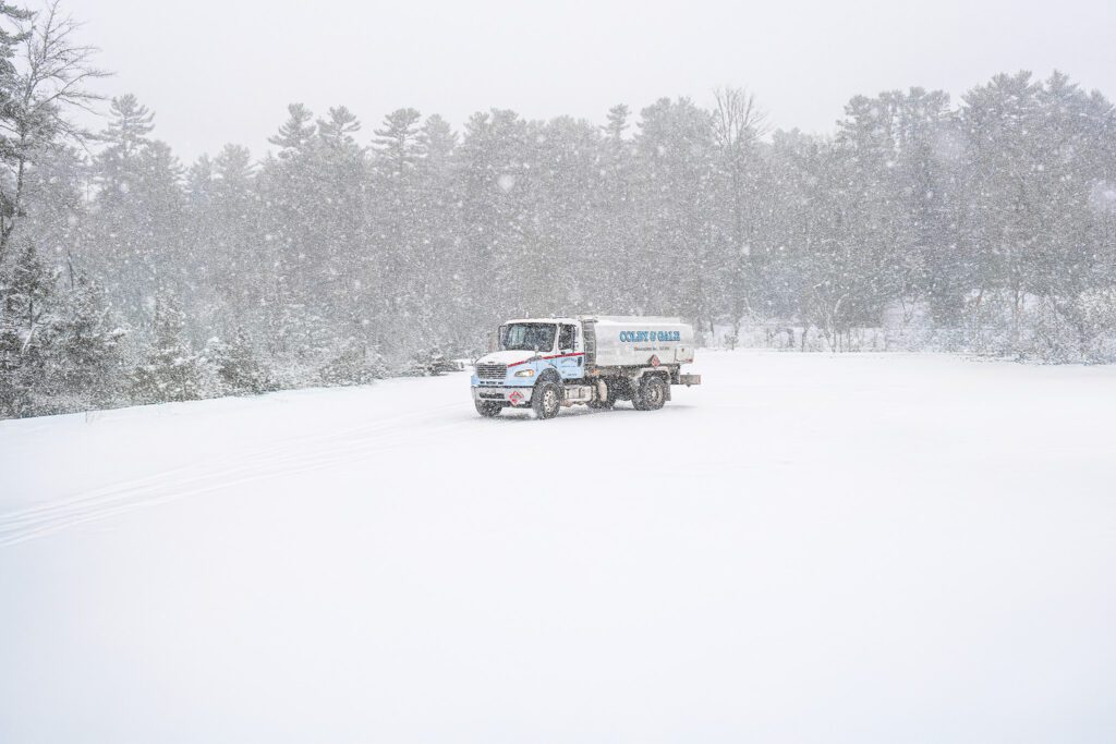 Heavy snow falls around a large silver oil truck with painted light blue letters spelling Colby & Gale