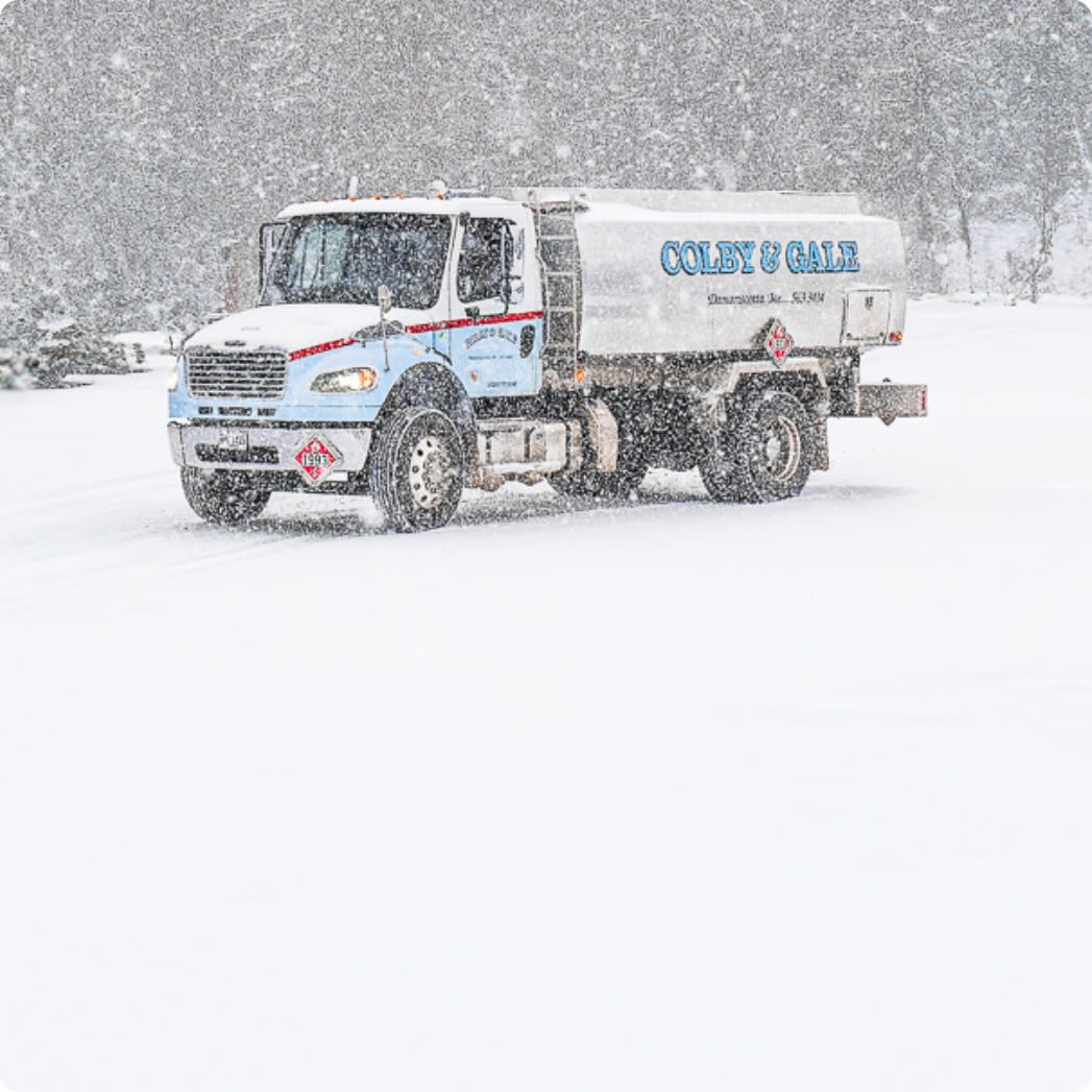 Heavy snow falls around a large silver oil truck with painted light blue letters spelling Colby & Gale