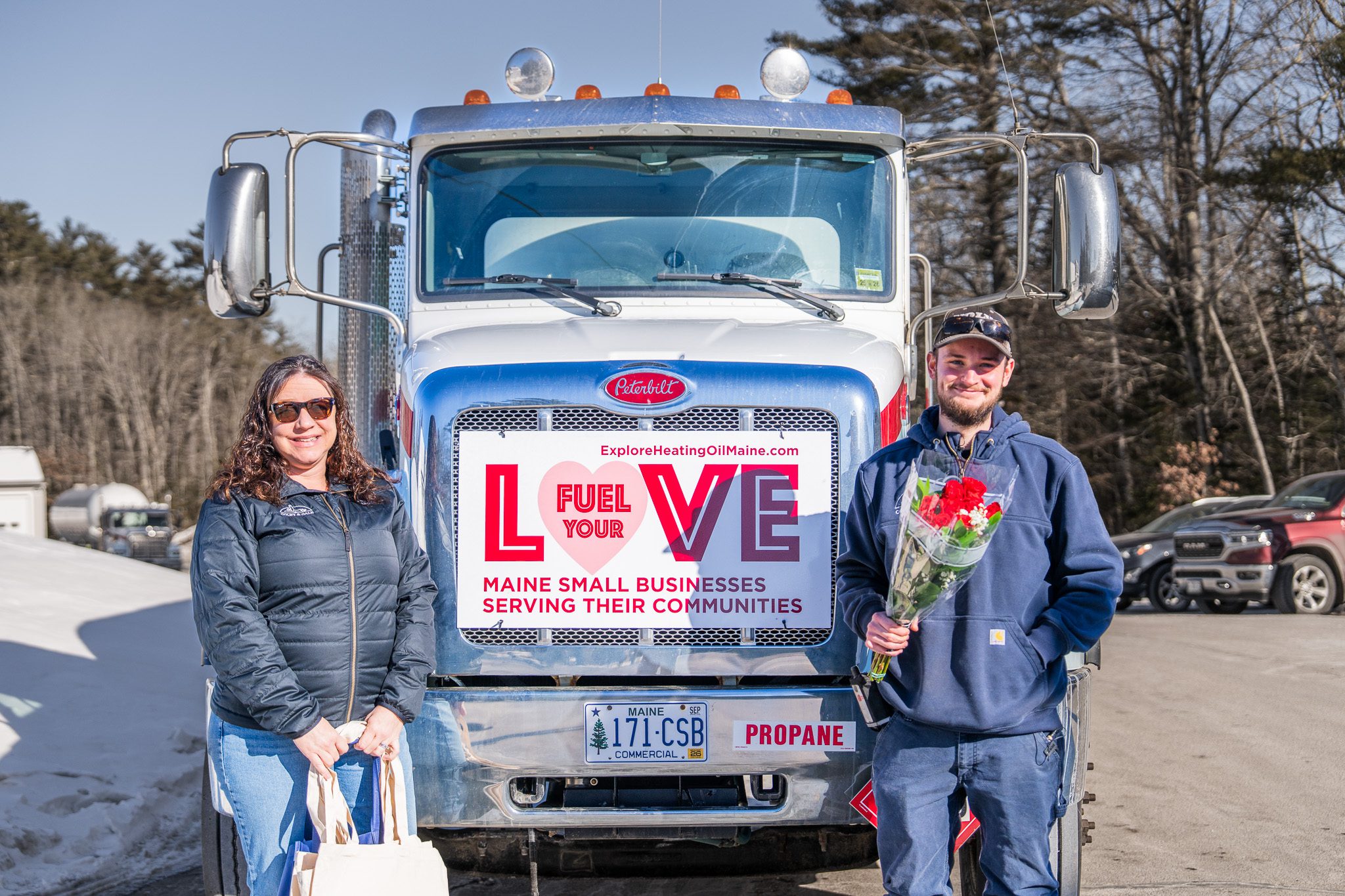 Amanda Reed and delivery driver Carter Frost standing in front of a Colby & Gale fuel truck with a "Fuel Your Love" sign displayed on the grille.