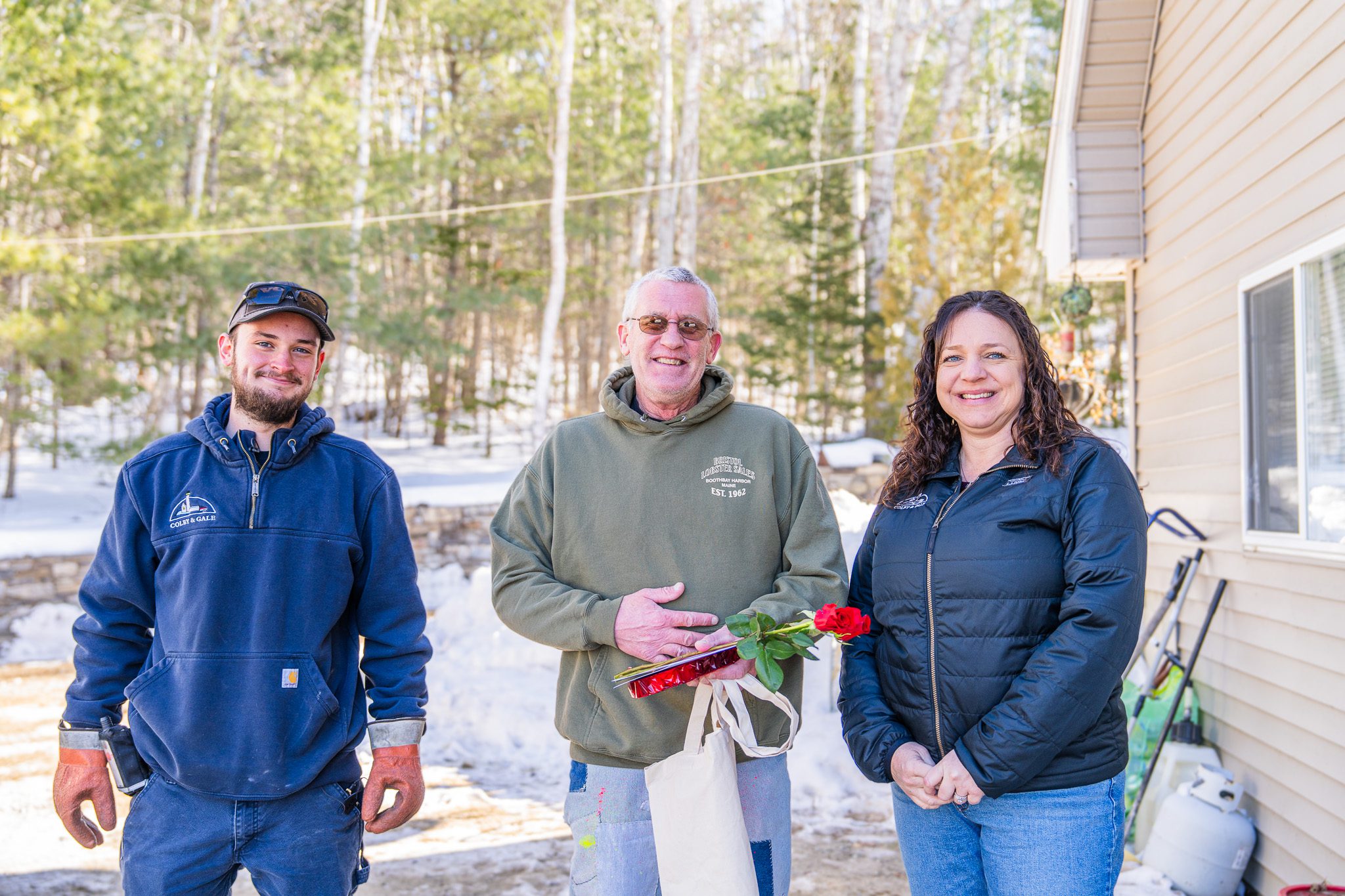Amanda Reed and delivery driver Carter Frost standing with a local resident in Boothbay during a Colby & Gale "Fuel Your Love" surprise delivery.