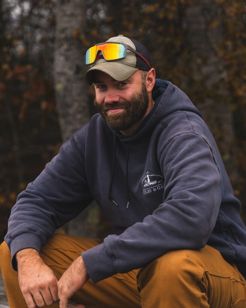 Dustin Creamer sitting with arms on knees and wearing a hat with sunglasses on them.