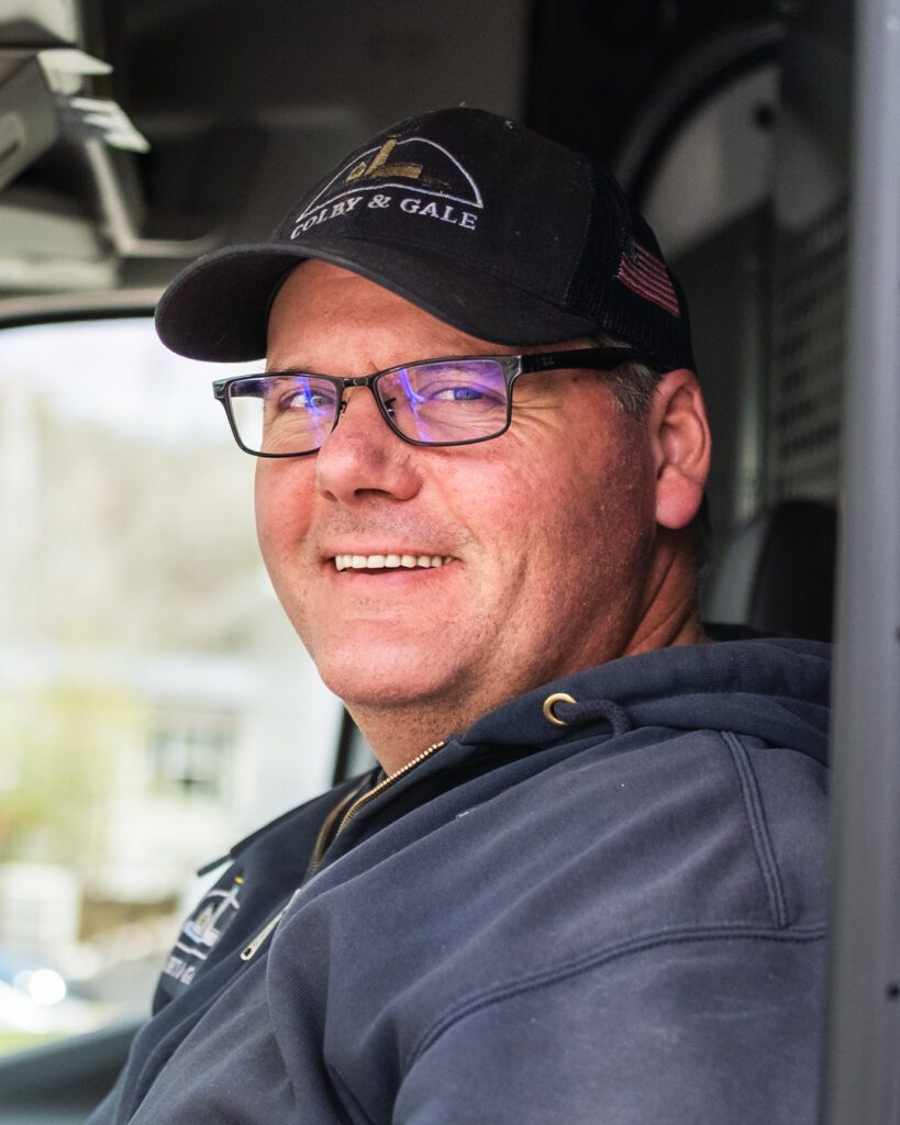 Gary Vallieres in driver side of service van wearing a hat and glasses, smiling.