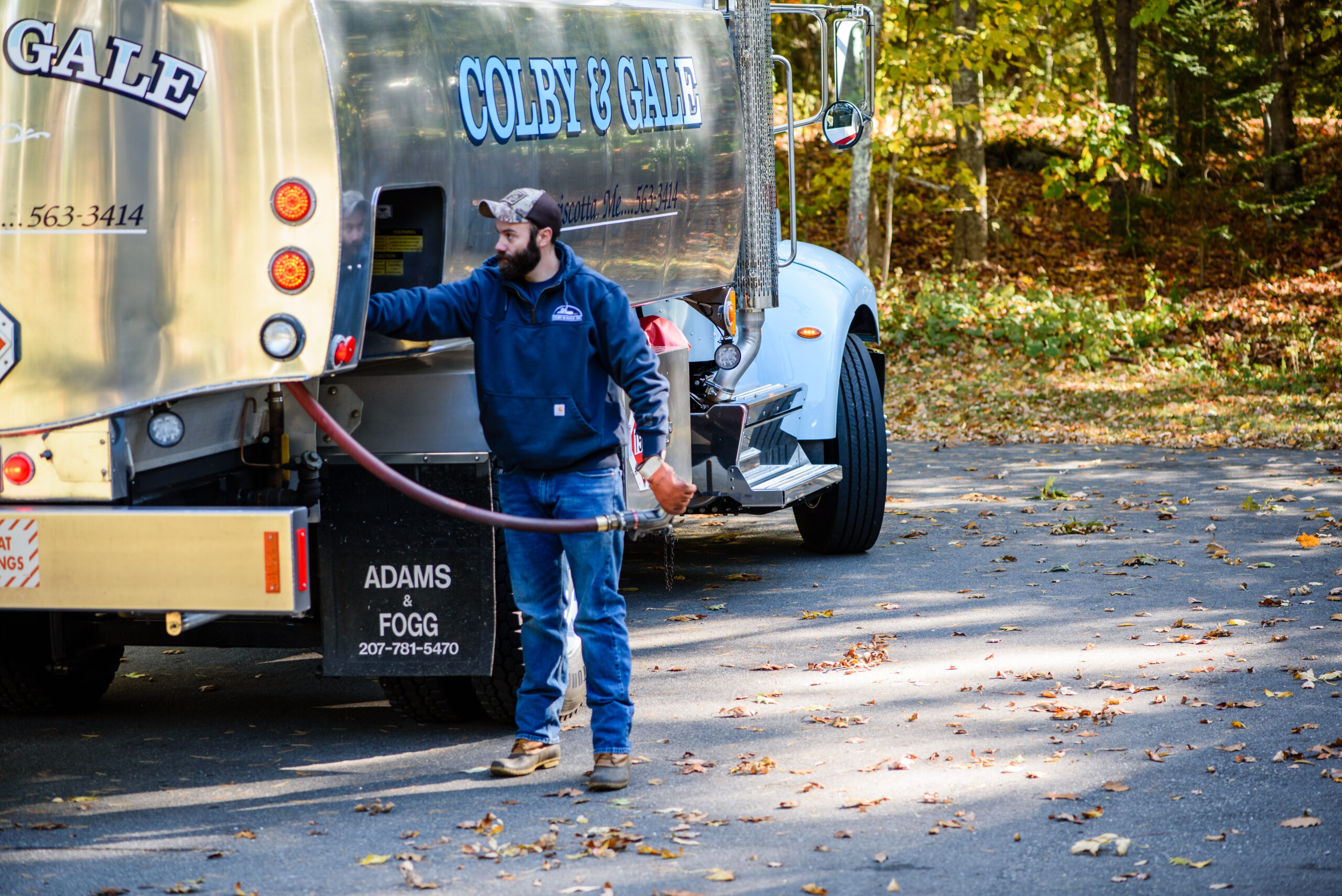 A man next to a fuel truck about to pull a fuel hose out of the side.