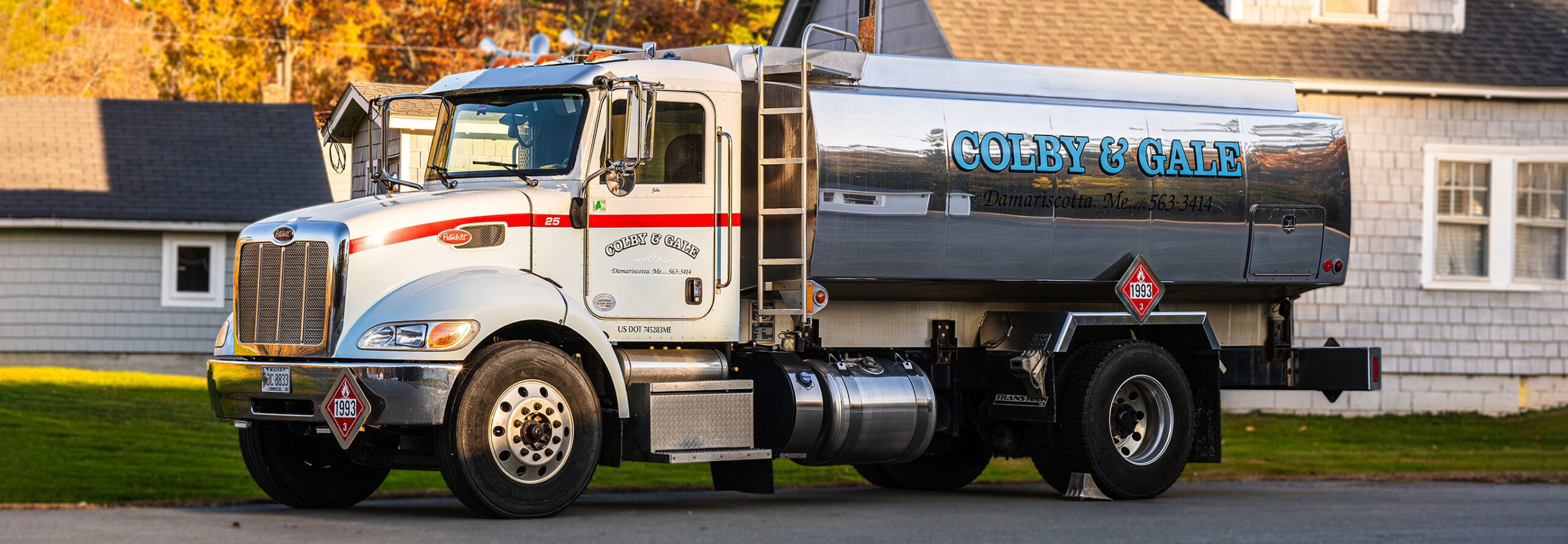 A shiny heating oil truck parked in front of a shingle style New England home.