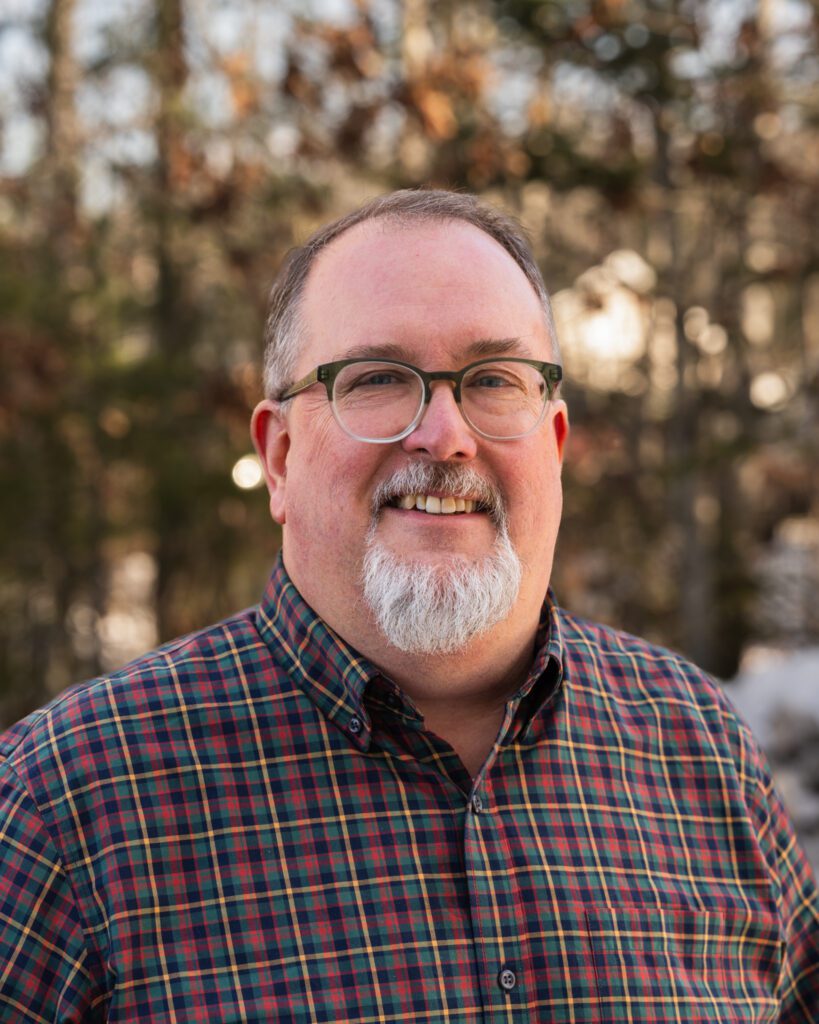 Jed Weiss, wearing glasses, and checkered shirt poses for camera