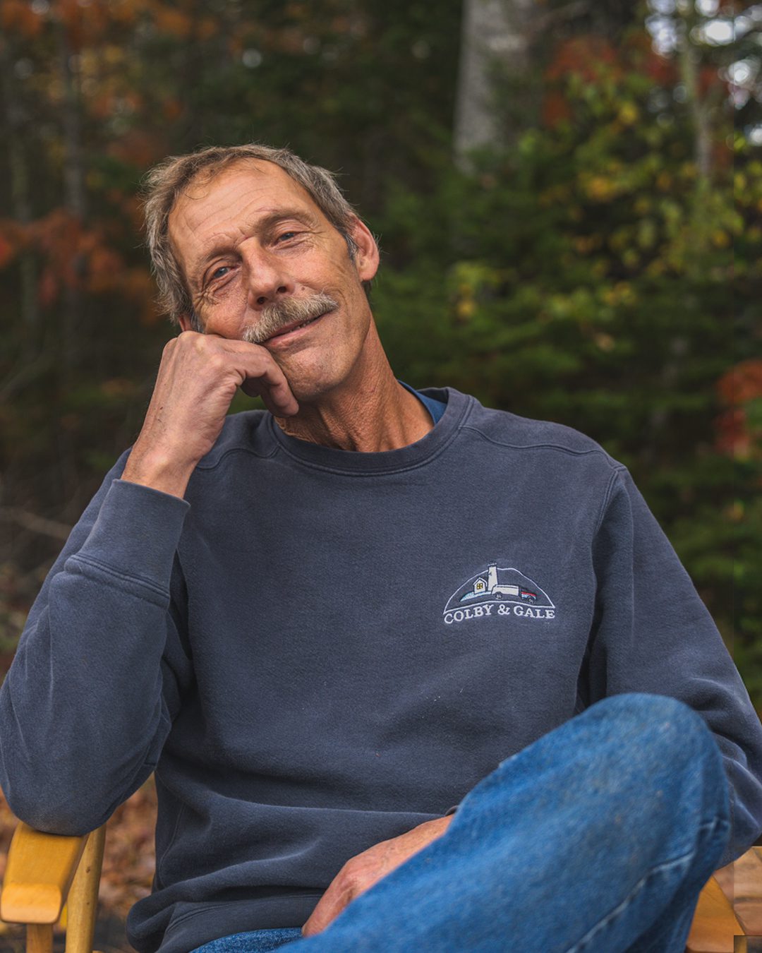John Murphy Sitting and smiling in chair with hand to his cheek.