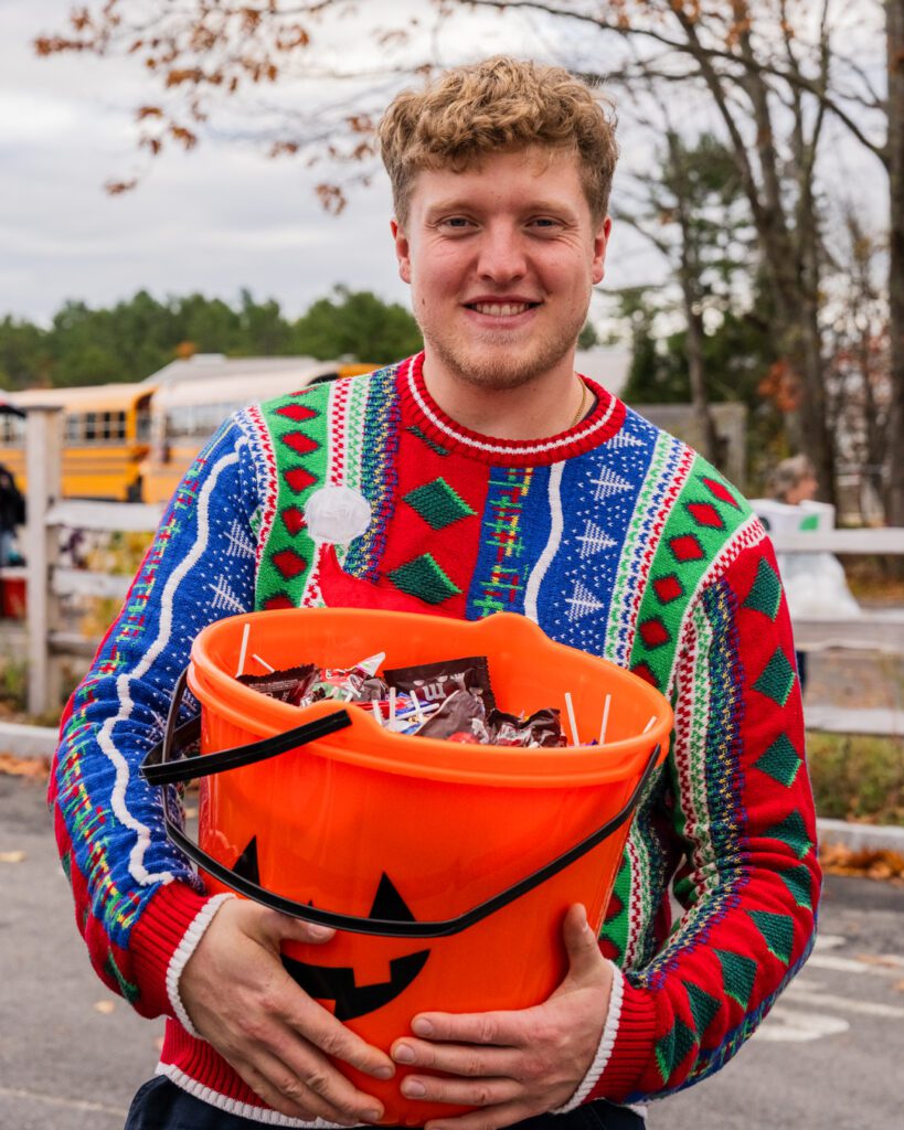 Noah Powell holding a Halloween bucket full of candy wearing a Christmas sweater.
