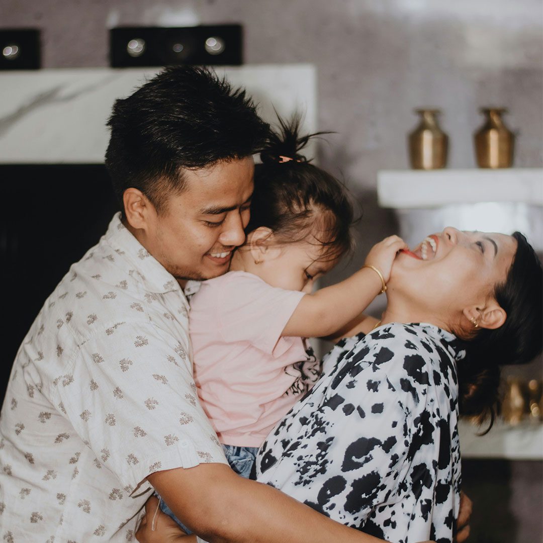 A family of three laughs with their small child.