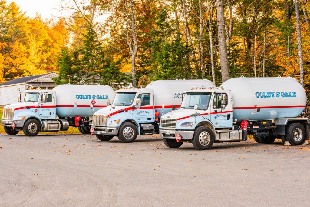 Three Colby & Gale trucks lined up in a row, with fall trees in the background