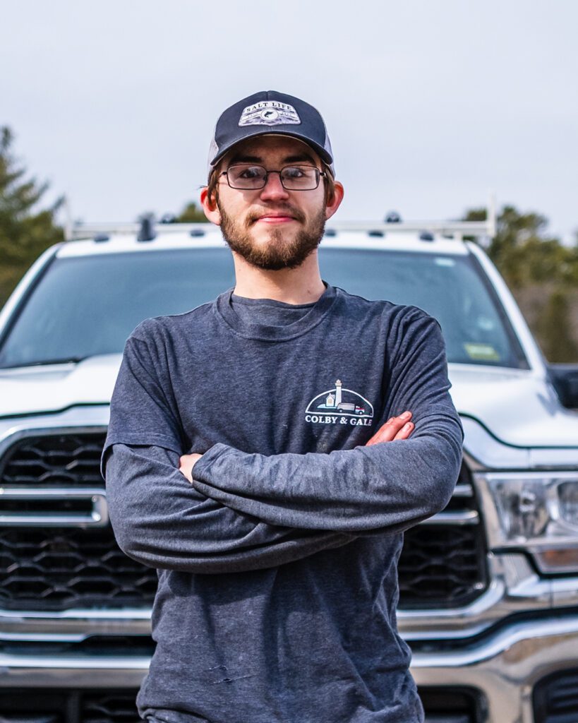 Tyler Donahue standing with arms crossed, wearing a Colby & Gale hat in front of a truck. 